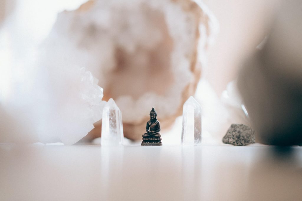 Two clear quartz crystals, a rock, and a small Buddha statue between the crystals