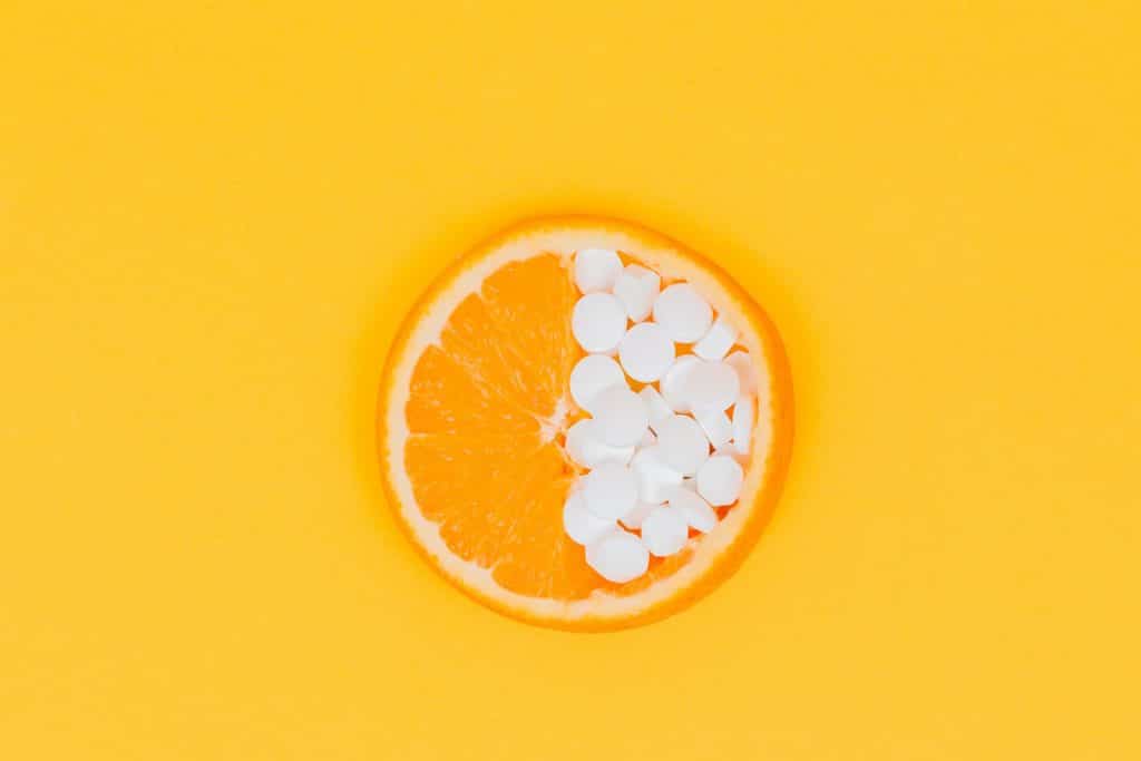 A circular slice of an orange and its right side covered with white vitamin pills